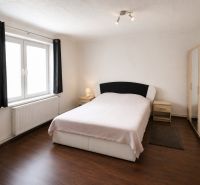 A bedroom in a family house with a wood-patterned floor, light, and furniture in neutral colors.