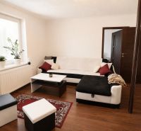 Living room with a corner sofa, wood-patterned flooring, and houseplants.