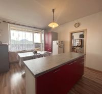 A kitchen in a three-room apartment with a wooden decor floor and red cabinets.