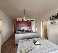 A kitchen in a 3-room apartment with a table, red cabinets, and a floor with a wood decor.