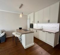 A kitchen in a 2-room apartment with an island, white cabinets, and a wood-patterned floor.