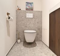 A toilet with decorative art, gray tiles, and wooden decor in a 3-room apartment.