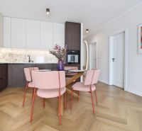Kitchen corner in a 3-room apartment with a table, pink chairs, and a wooden decor floor.