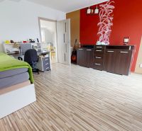 Interior of a family house with a bed, a desk, and a wooden-patterned floor.