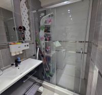 A bathroom with a shower, sink, and tiled walls in a 4-room apartment.