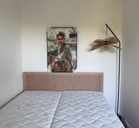 Bedroom in a studio apartment with a picture above the bed and a hanging lamp.