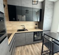 A kitchen with black and gray cabinets, a wood-patterned floor, and a dining table in a studio apartment.