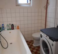 A family house bathroom with a bathtub, a washing machine, and tiles on the wall.