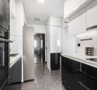 A kitchen in a 2-room apartment with black and white cabinets and marble tiles.