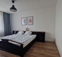 A bedroom in a two-room apartment with a wooden decor floor, a bed, and pictures on the wall.