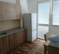 A kitchen in a 2-room apartment with a wooden decor floor and a table with chairs.
