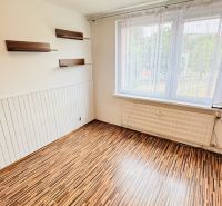 A room with a wooden decor floor, shelves, and a large window in a 3-room apartment.