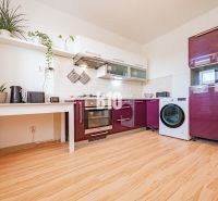 A kitchen with white shelves, a modern countertop, and a wooden decor floor in a studio apartment.