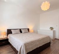Bedroom in a 2-room apartment with a bed, dresser, and wooden decor flooring.