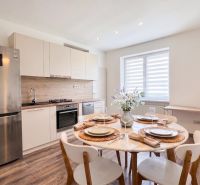 A kitchen of a two-room apartment with a wooden decor floor, a dining table, and appliances.