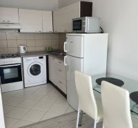 A kitchen in a studio apartment with a kitchenette, refrigerator, and wooden decor flooring.