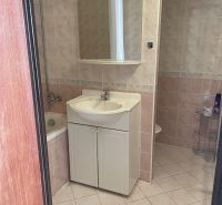 A bathroom in a studio apartment with a sink, bathtub, and ceramic tiles.