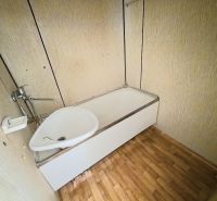 A bathroom in a studio apartment with a bathtub and a wooden decor floor.