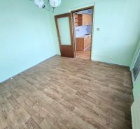 A room in a one-room apartment with a wooden decor floor and a transition to the kitchen.