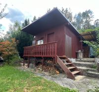 A wooden cottage in the Gardens of Ružomberok surrounded by greenery and trees on a slope.