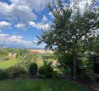Gardens in Ružomberok with a view of the mountains, with trees and cottages under a blue sky.