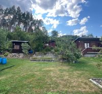 Cottages surrounded by greenery in gardens in Ružomberok under a blue sky with clouds.