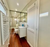 A bathroom with a mirror, sink, radiator, and floor with a wooden decor in Záhrady.