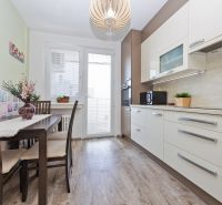 A kitchen with a table, light cabinets, and a wooden decor floor in a 3-room apartment.