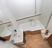 Bathroom with a shower tub, sink, tiles, and a wooden decor floor in a 3-room apartment.