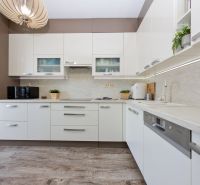 A kitchen with white cabinets, appliances, and a wood-patterned floor in a three-room apartment.