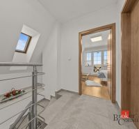 Hallway with a staircase and doors leading to a room with wood-patterned flooring.