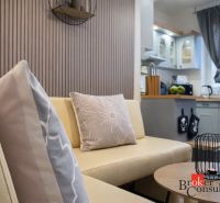 Interior of a 3-room apartment with a beige sofa and a kitchen in the background.