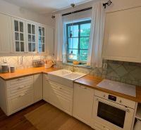A kitchen in a family house with white cabinets, wooden decor, and a blue window.