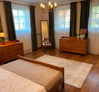 A bedroom with wooden furniture, a floor with a wooden decor, and large windows in a family house.