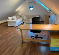 Attic space with a desk, sofa, and wooden decor flooring in a family house.