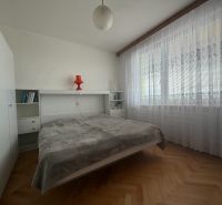 Bedroom in a 2-room apartment with wood-patterned flooring and large windows.