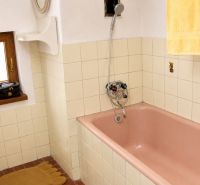A bathroom in a cottage with a pink bathtub, beige tiles, and a small window.