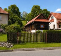 A cottage in Beňadiková surrounded by greenery, red roofs, wooden fence, paved road.
