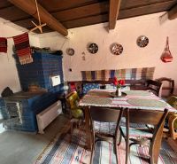 Rustic interior of a cottage with a blue stove, wooden ceiling, and decorated table.