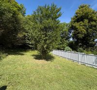 A grassy plot near a cottage in Beňadiková with trees and a fence in a sunny location.