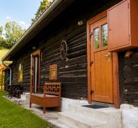 Wooden cottage in Beňadiková with wooden doors, a bench, and surrounding greenery.