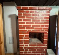 A brick fireplace in a cottage with a wooden ceiling and a floor with a wooden decor.