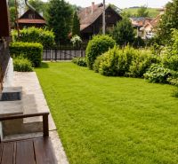 The garden of the cottage in Beňadiková with a lawn and wooden structures in the background.