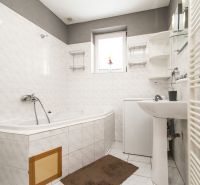 A bathroom in a family house with a bathtub, sink, and washing machine, tiled with white tiles.