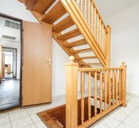 Wooden staircase and tiles in the interior of a family house with rooms in the background.