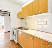 A kitchen in a 2-room apartment with a wooden decor floor and a simple kitchen unit.
