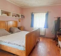 A bedroom in a family house with simple furniture, a bed, and shelves, a floor with a wooden decor.