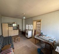 A room in a cottage with older furnishings; a sofa, a table, and a cupboard.