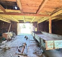 An interior view of a cabin with an old wooden structure, a trailer, and farming tools.
