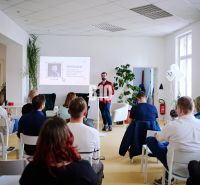 A lecture in the office, participants sitting on chairs, presentation projected on the wall.